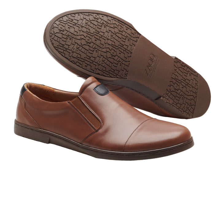 Ein Paar CLARQ Brown-Slipper von ZAQQ, gefertigt aus luxuriösem Nappaleder. Ein Schuh steht aufrecht, der andere ist geneigt, um ein strukturiertes Griffmuster sowie das ZAQQ-Branding auf der Sohle zu präsentieren. Das Design verbindet nahtlos lässigen Stil mit alltäglicher Eleganz und eignet sich daher perfekt für Geschäfts- und Freizeitumgebungen.