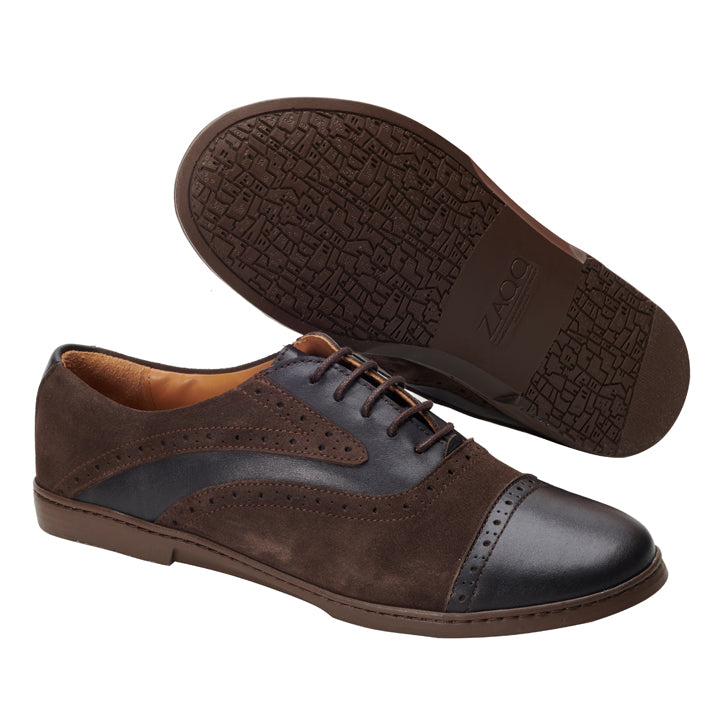 Wir präsentieren den QENTLE Dark Brown von ZAQQ: ein Paar stilvolle Oxfords für Herren aus braunem Wildleder mit Akzenten aus dunklem Leder. Ein Schuh steht aufrecht und hebt seine Brogue-Details hervor, während der andere umgedreht ist und die strukturierte Sohle zeigt. Perfekt für alle, die einen Businessschuh mit elegantem Touch suchen.