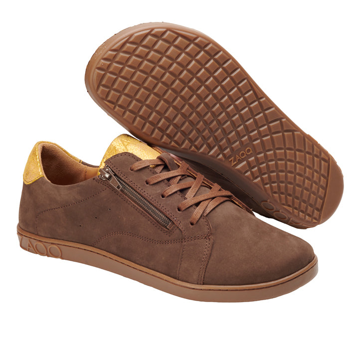 Wir präsentieren den QOMFY Wide Brown von ZAQQ, ein stilvolles Paar brauner Sneaker mit Wildleder-Finish. Diese Schuhe verfügen über praktische seitliche Reißverschlüsse und einen auffälligen Kontrast mit ihrem gelben Fersenakzent. Als Barfußschuhe konzipiert, bieten sie dank ihrer extra breiten Gummisohle mit Gitterprofil außergewöhnlichen Tragekomfort. Der erkennbare Markenname ZAQQ ist sowohl an der Seite als auch an der Sohle der Sneaker deutlich sichtbar.