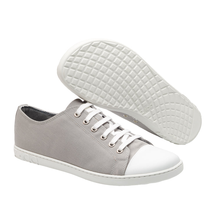 Die CHUQQS Low Grey Sneaker von ZAQQ bestechen durch ihr lässiges, minimalistisches Design mit hellgrauem Stoff und weißen Gummisohlen und Zehenkappen und sind damit ideal für einen urbaneren Stil. Ein Schuh steht aufrecht, während der andere geneigt ist, um die gemusterte Sohle zu präsentieren. Die weißen Schnürsenkel verleihen diesen vielseitigen Kicks einen klassischen Touch.