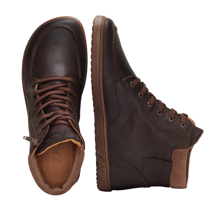 Ein Paar ROQA Brown High-Top-Sneaker von ZAQQ wird nebeneinander ausgestellt, einer aufrecht und der andere geneigt, wodurch der auf der Seitensohle eingeprägte Markenname ZAQQ hervorgehoben wird. Diese Schuhe sind als Barfußschuh aus dunkelbraunem Nappaleder mit braunen Schnürsenkeln konzipiert und versprechen hohen Tragekomfort für den ganzen Tag.