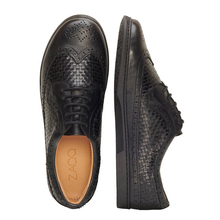 Die BRIQ Brogue Tresse Black von ZAQQ sind schwarze Lederschnürschuhe mit einer exquisiten gewebten Textur und dekorativen Perforationen an der Spitze. Ein Schuh ist von oben abgebildet und zeigt den Markennamen ZAQQ, während der andere von der Seite gezeigt wird.