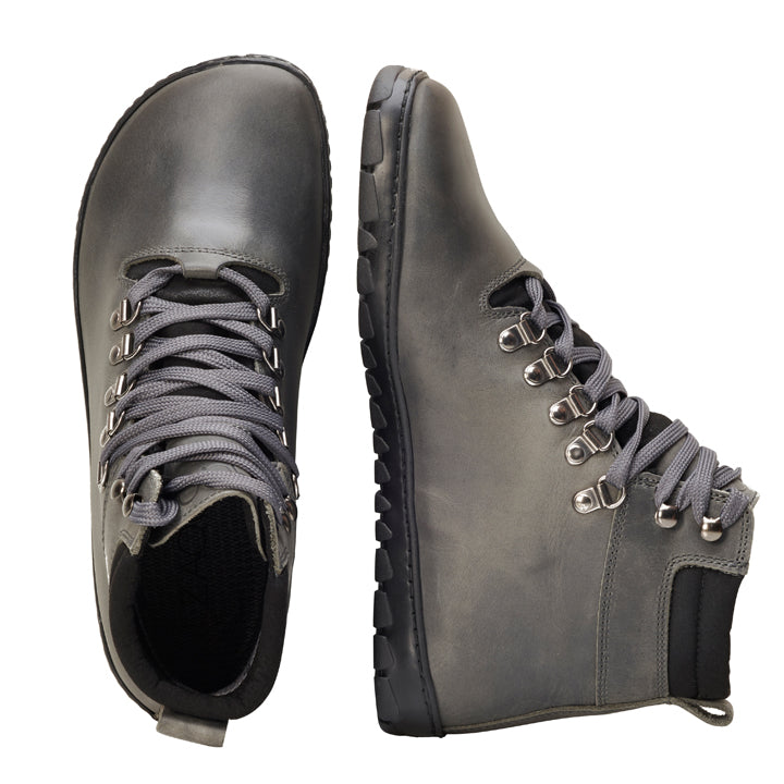 Die ZAQQ EXPEQ Wide Grey Waterproof High-Top-Wanderschuhe sind mit Metallösen und robusten grauen Schnürsenkeln ausgestattet. Diese strapazierfähigen Barfußschuhe haben eine schwarze Sohle, die hervorragenden Halt und lange Haltbarkeit bietet. Ein Schuh wird von oben präsentiert, während der andere sein Seitenprofil hervorhebt und sein zuverlässiges wasserdichtes Design zur Schau stellt.