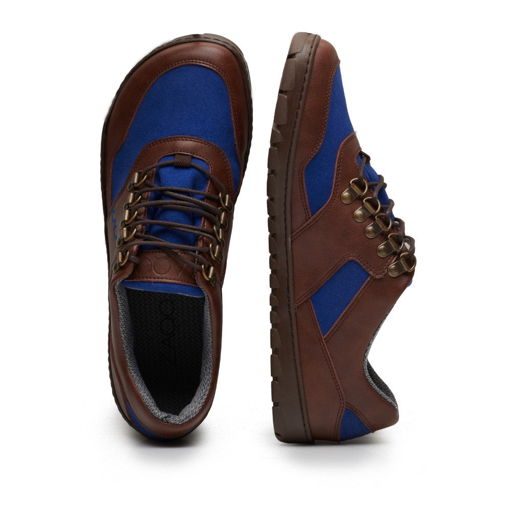 Wir präsentieren den HIQE Low Brown Blue Waterproof von ZAQQ: Ein Paar braun-blaue Freizeit-Sneaker aus veganen Materialien. Diese Schuhe haben dunkelbraune Schnürsenkel, eine robuste strukturierte Sohle und sind aus einer Mischung aus lederähnlichen und Stoffmaterialien gefertigt. Sie sind mit Metallösen für die Schnürsenkel versehen und werden sowohl von der Seite als auch von vorne präsentiert.