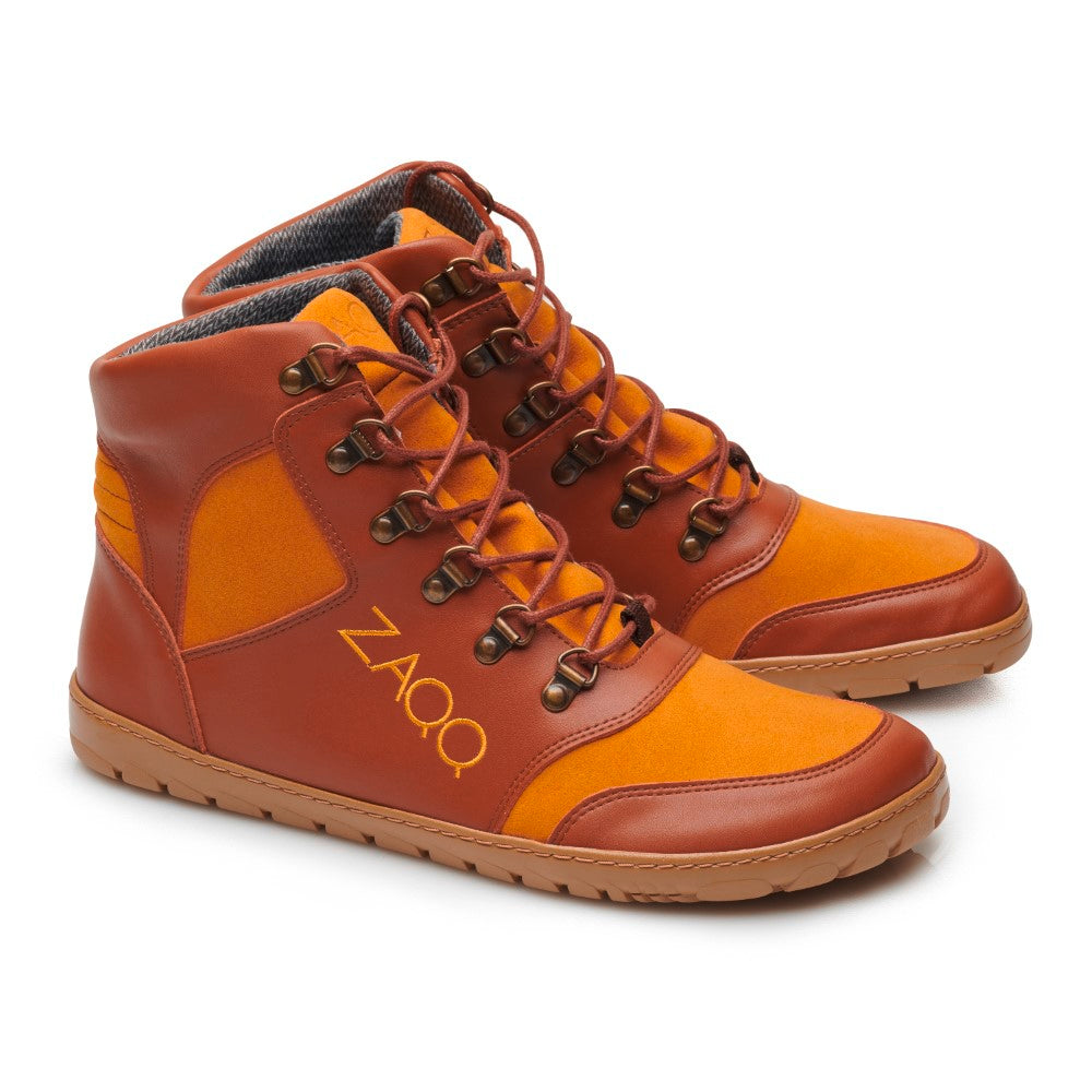 Der HIQE Vegan Sierra Waterproof Sneaker von ZAQQ ist ein Paar High-Top-Schuhe in Orange- und Brauntönen, die ähnlich vielseitig sind wie vegane Wanderschuhe. Diese Sneaker haben Schnürungen vorne, kontrastierende Einsätze, eine Seite mit dem gelben „ZAQQ“-Logo und robuste Sohlen – alles auf weißem Hintergrund.