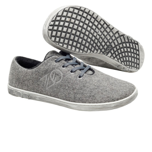 Die LIQE Grey Sneaker von ZAQQ haben dunkle Schnürsenkel und strukturierte Gummisohlen. Diese temperaturregulierenden Schuhe haben ein schlichtes Design mit einem dezenten Logo an der Seite und Branding auf der Sohle. Ein Schuh ist von der Seite zu sehen, während der andere von unten zu sehen ist.