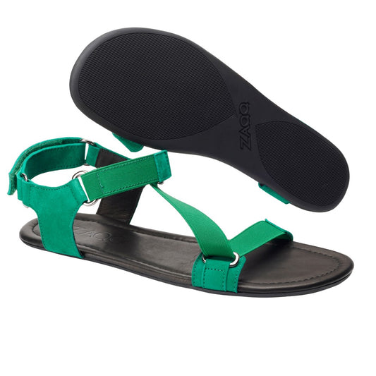 Ein Paar ZAQQ MIQA Green Sandalen mit Riemchensystem mit verstellbaren Riemen und schwarzer Sohle. Eine Sandale steht aufrecht und zeigt die Textur der Sohle, während die andere flach als Barfußsandale liegt, um ihr Design hervorzuheben.