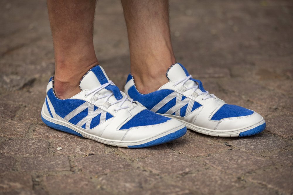 Zwei Füße in den blauen Sport-Sneakers „QENDRIQ Blue“ von ZAQQ ruhen auf einem Ziegelsteinpflaster und verströmen einen knackigen und stilvollen Look.