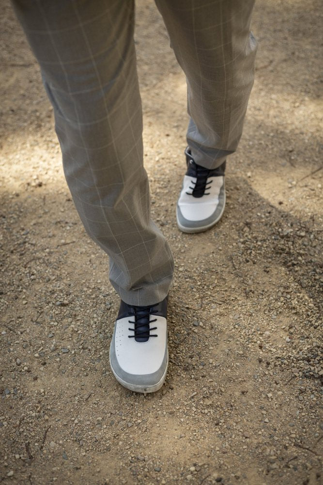 Eine Person in grau karierten Hosen und QOOL Navy-Sneakern von ZAQQ mit schwarzen Schnürsenkeln schreitet einen Feldweg entlang und genießt höchsten Komfort.