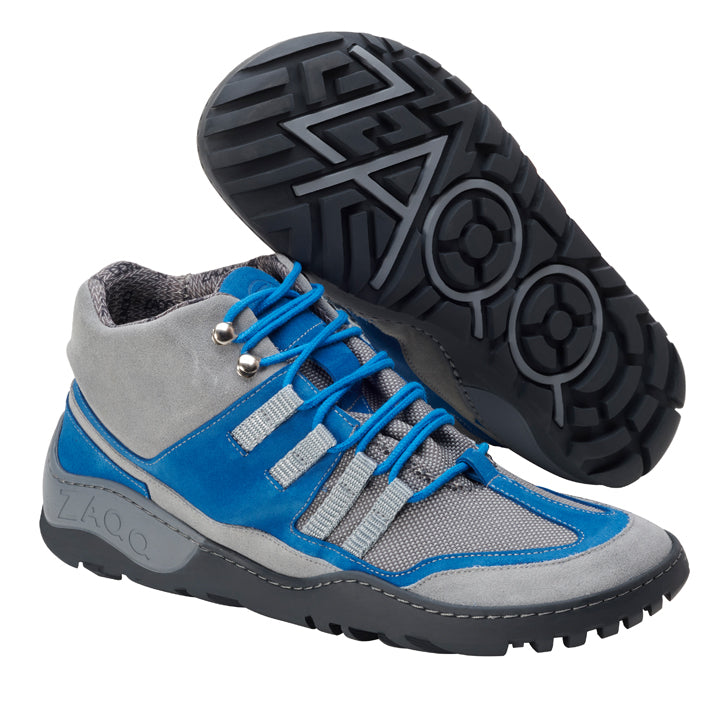 Der SQOUT Grey Blue Waterproof von ZAQQ besticht durch ein stylisches Barfußschuh-inspiriertes Design in Blau, Grau und Silber. Der Wanderschuh hat eine atmungsaktive, robuste Sohle mit geometrischem Muster und einen Schnürverschluss. Der Markenname ZAQQ ist prominent auf der Seite angebracht.