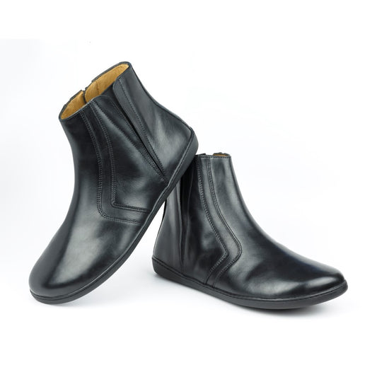 Ein Paar elegante SQY-Stiefeletten aus schwarzem Leder von ZAQQ mit seitlichem Reißverschluss auf weißem Hintergrund. Die Stiefel erinnern an die klassische Eleganz von ZAQQ. Einer steht aufrecht, während der andere geneigt ist, um ihr glänzendes Finish und die detaillierten Nähte zu präsentieren.