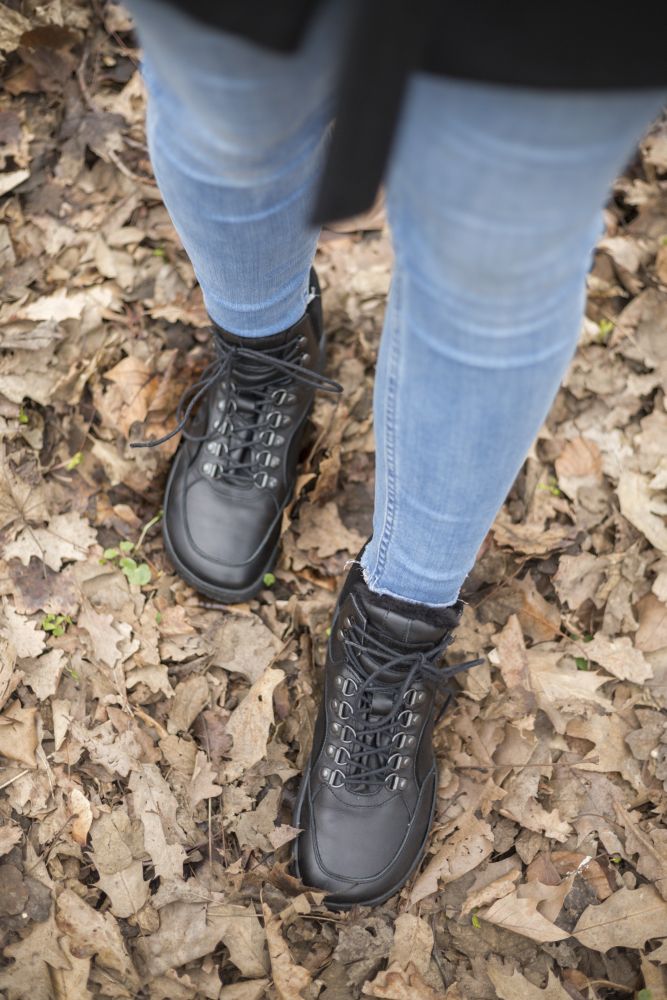 Eine Person in Blue Jeans und einem Paar wasserdichter TREQ Black Winter-Stiefel von ZAQQ steht auf einem mit braunen Blättern bedeckten Boden.