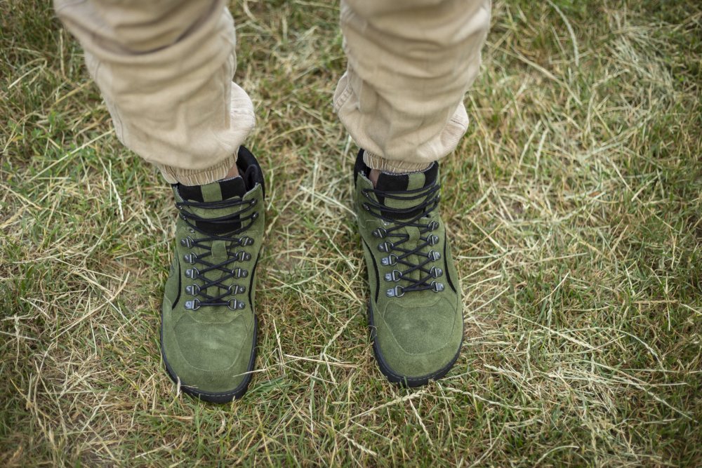 Eine Person, die TERRAQ Green Waterproof-Wanderschuhe von ZAQQ und eine beige Hose trägt, steht auf Gras.