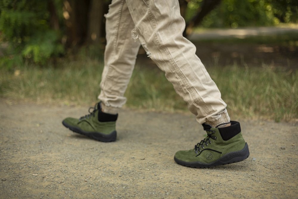 Eine Person läuft auf einem Schotterweg in hellbraunen Hosen und den TERRAQ Green Waterproof Wanderschuhen von ZAQQ. Im Hintergrund sind Bäume und Gras zu sehen.