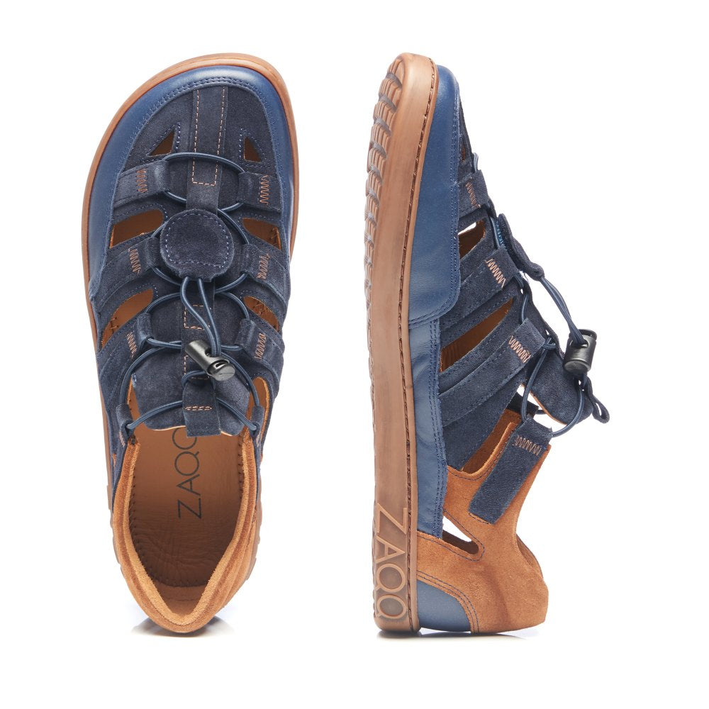 Wir präsentieren die QERRY Blue Cognac, ein Paar stylische ZAQQ-Sandalen in Blau und Braun mit Cut-Out-Design und verstellbaren Gummibändern, perfekt für Outdoor-Abenteuer. Diese Barfußschuhe aus Veloursleder haben strukturierte Sohlen mit dem Markennamen ZAQQ, der elegant auf der Seite angebracht ist.