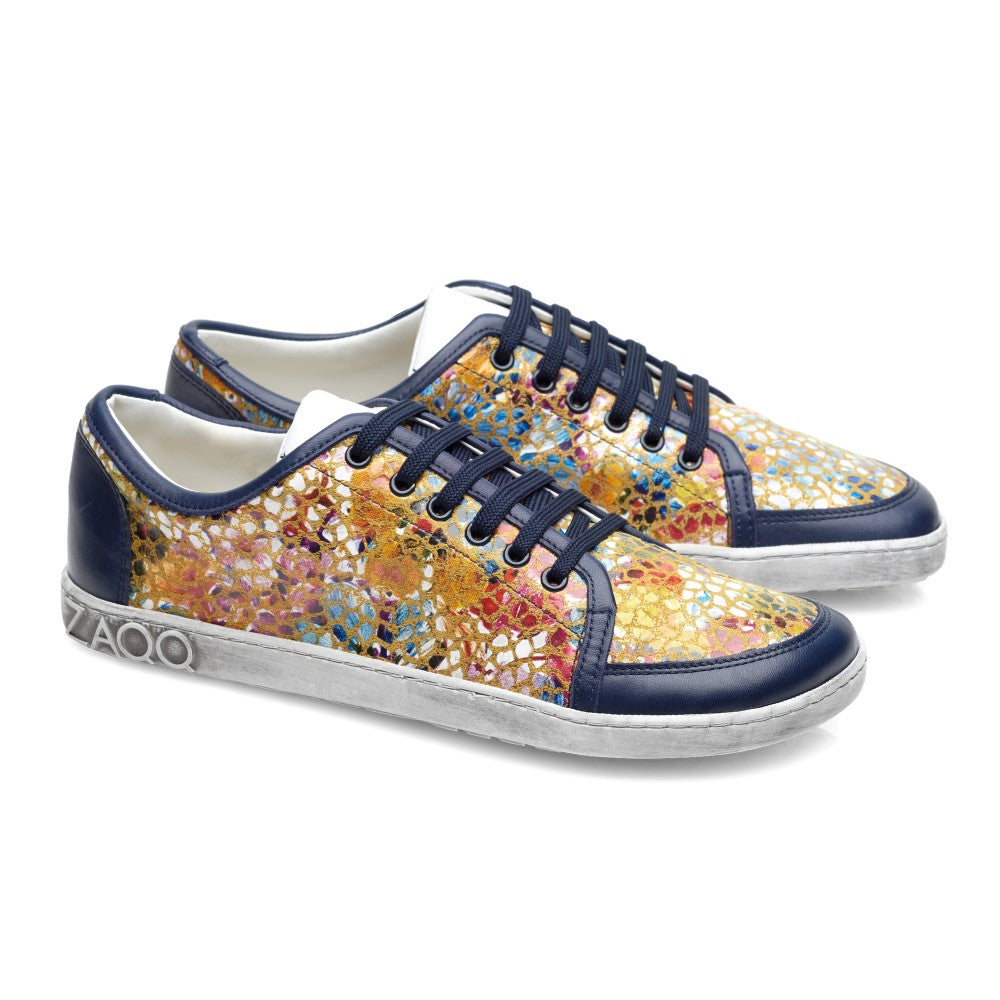 Wir präsentieren die farbenfrohen ZAQQ TIQQ Sneakers: Diese farbenfrohen Schuhe zeigen ein auffälliges Mosaikmuster in Blau, Gold und Orange an den Seiten, ergänzt durch marineblaue Schnürsenkel und Verzierungen. Sie sind aus hochwertigem Nappaleder gefertigt und verfügen über eine rutschfeste Sohle für mehr Stabilität. Die weißen Sohlen zeigen deutlich den geprägten Markennamen an der Ferse.